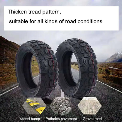 Two off-road tires with thick tread pattern on a road with mountainous background