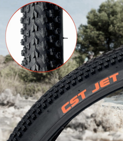 Close-up of a CST Jet bicycle tire with tread pattern detail and blurred natural background